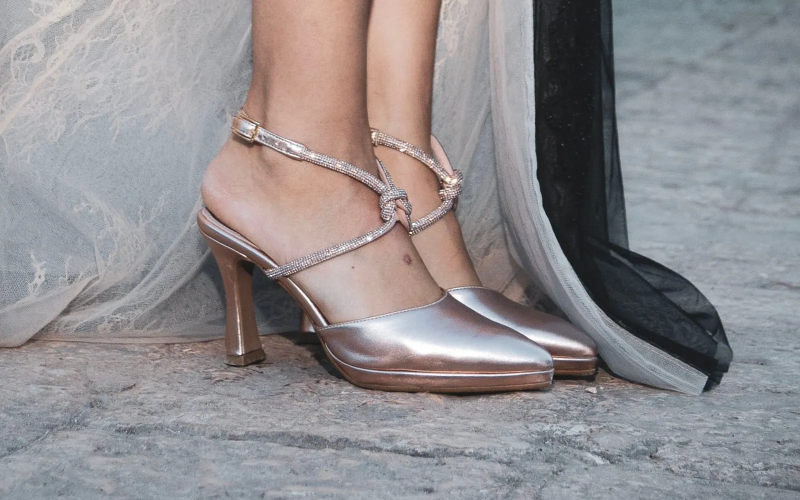 Chaussures rose métallisé avec bride de strass nouée à la cheville, près de l'ourlet d'une robe en dentelle et tulle